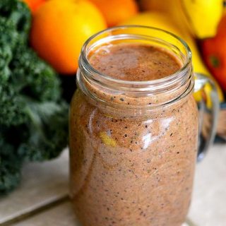 Speckled Strawberry Smoothie in a glass jar in front of fresh fruit and kale
