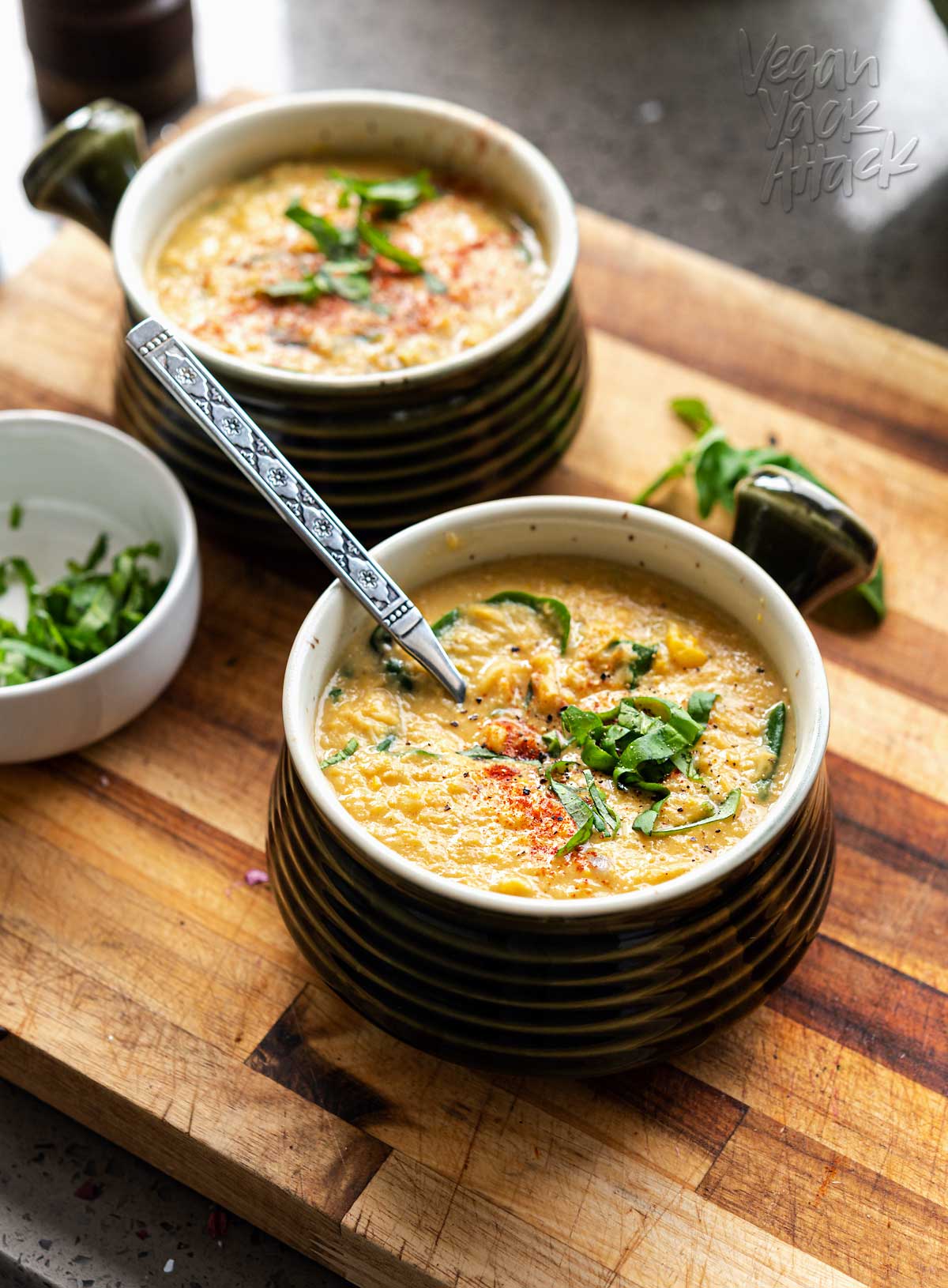 Bowls of corn chowder topped with basil on a cutting board