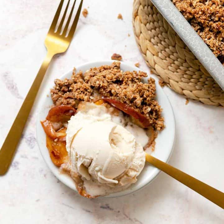 A small plate with a scoop of ice cream and scoop of apple pear crisp with gold forks