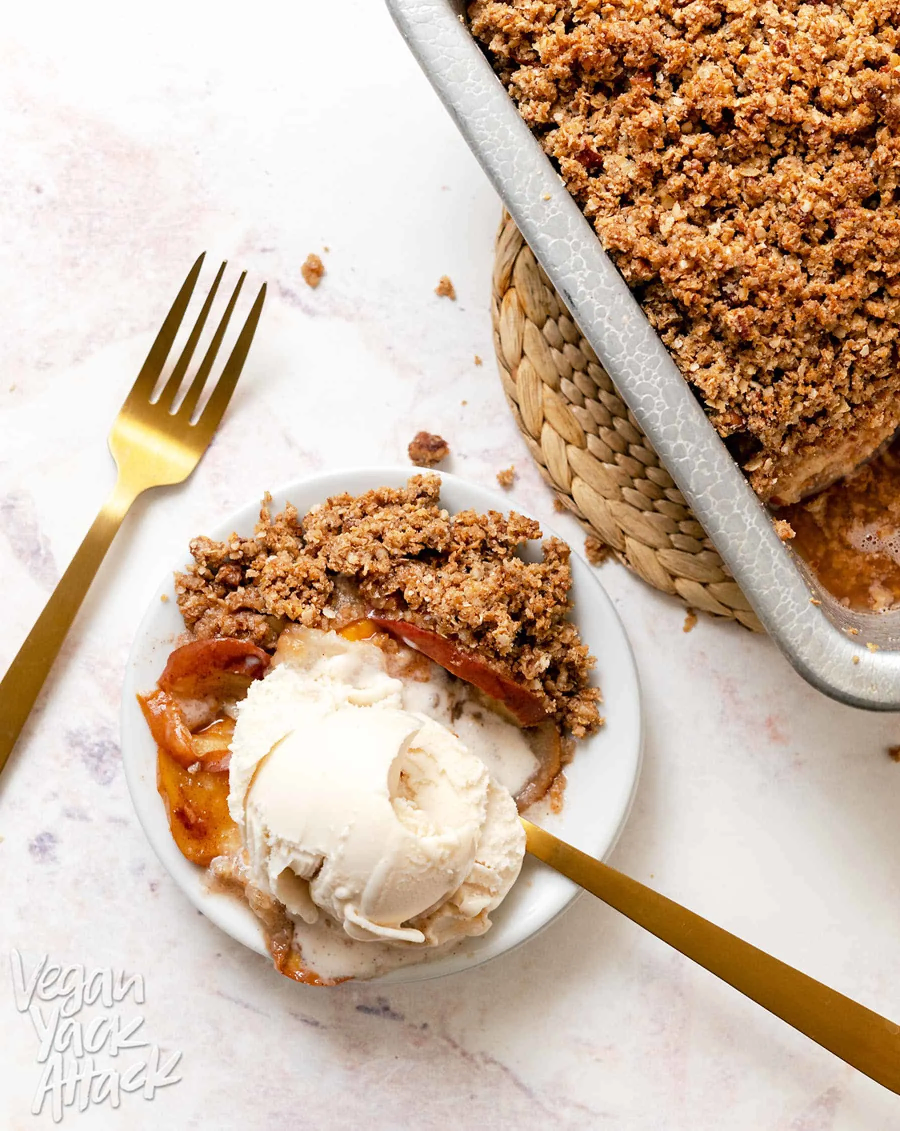 A small plate with a scoop of ice cream and scoop of apple pear crisp with gold forks