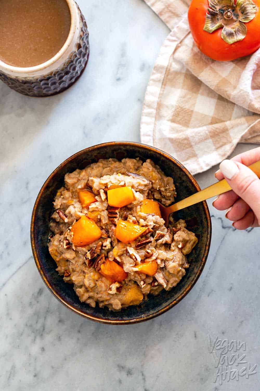Ceramic bowl filled with persimmon oatmeal, and golden spoon, with a cup of coffee