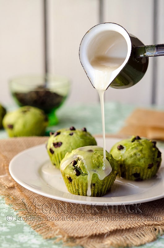 Glaze being poured over green-hued, chocolate chip cupcakes on a white plate
