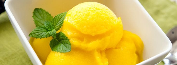 Mango lime sorbet in a white bowl with mint garnish