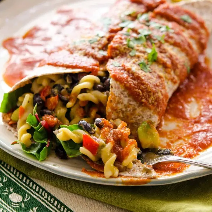 A large burrito stuffed with Mac and cheese and topped with red sauce