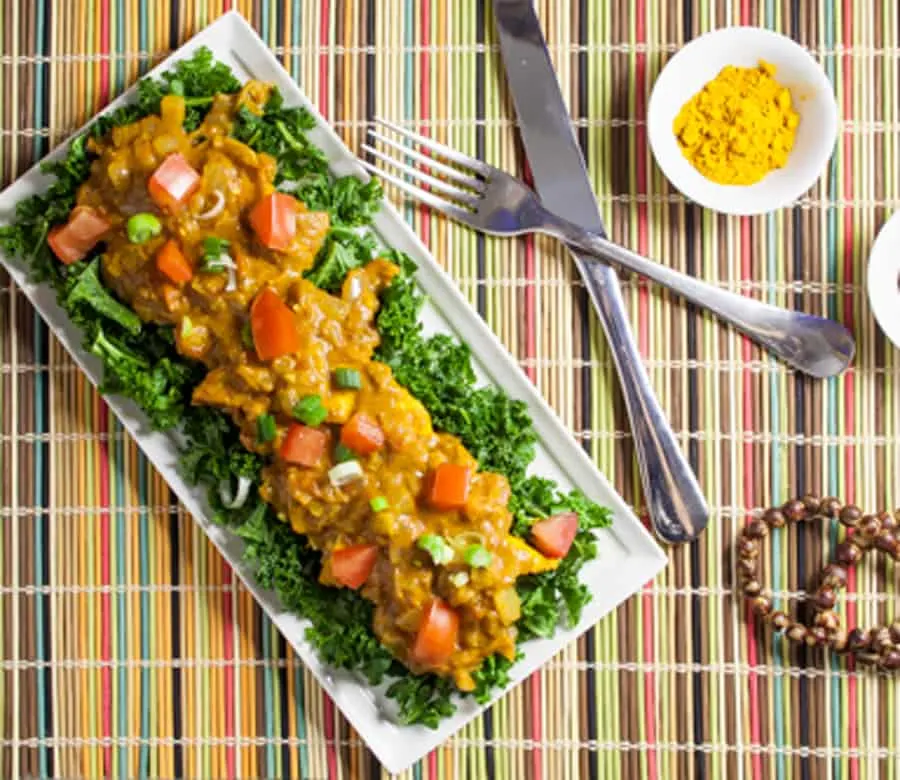 rectangular plate of steamed kale topped with Indian Butter Tofu, on a colorful placemat