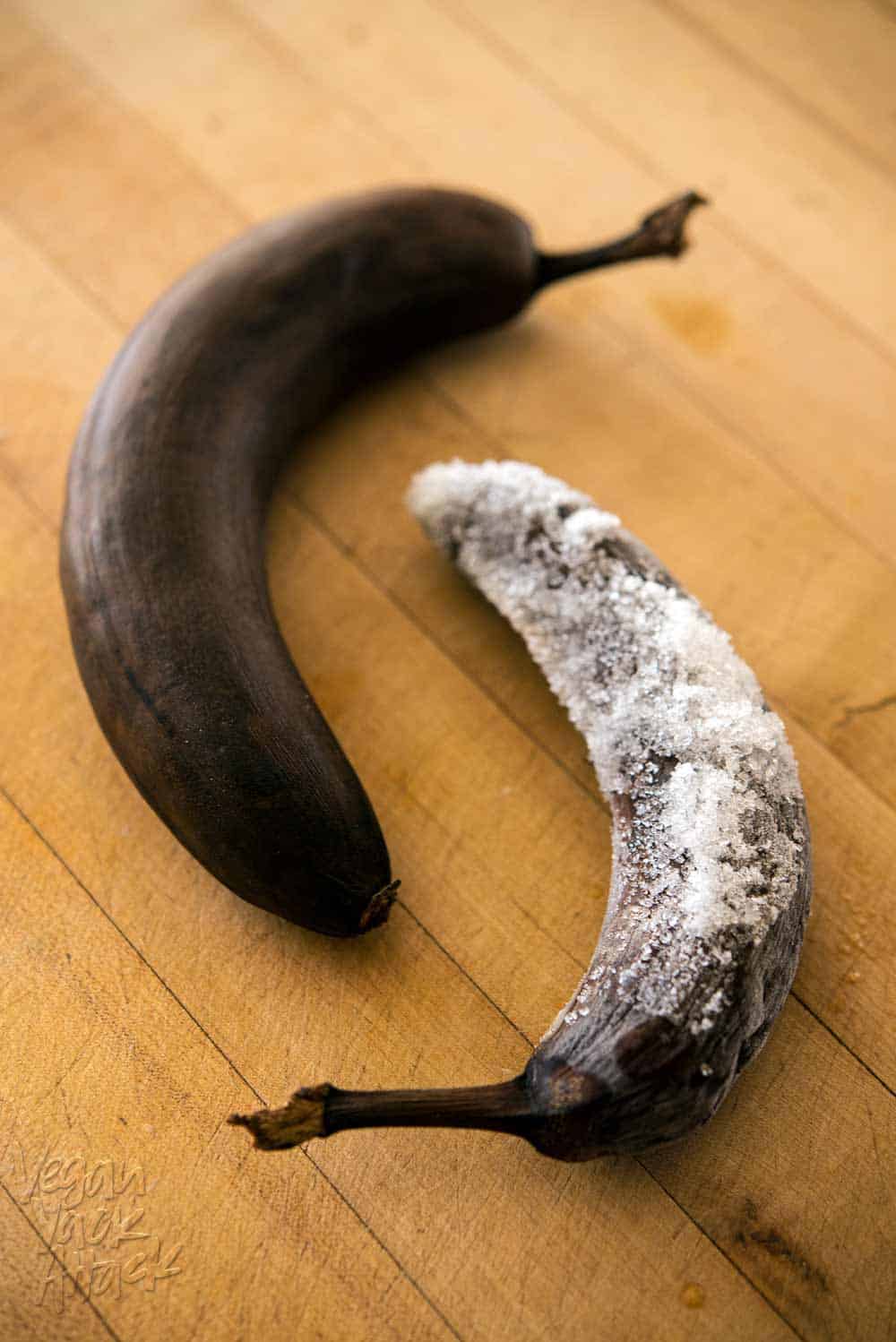 two very ripe bananas on a cutting board, one covered in ice