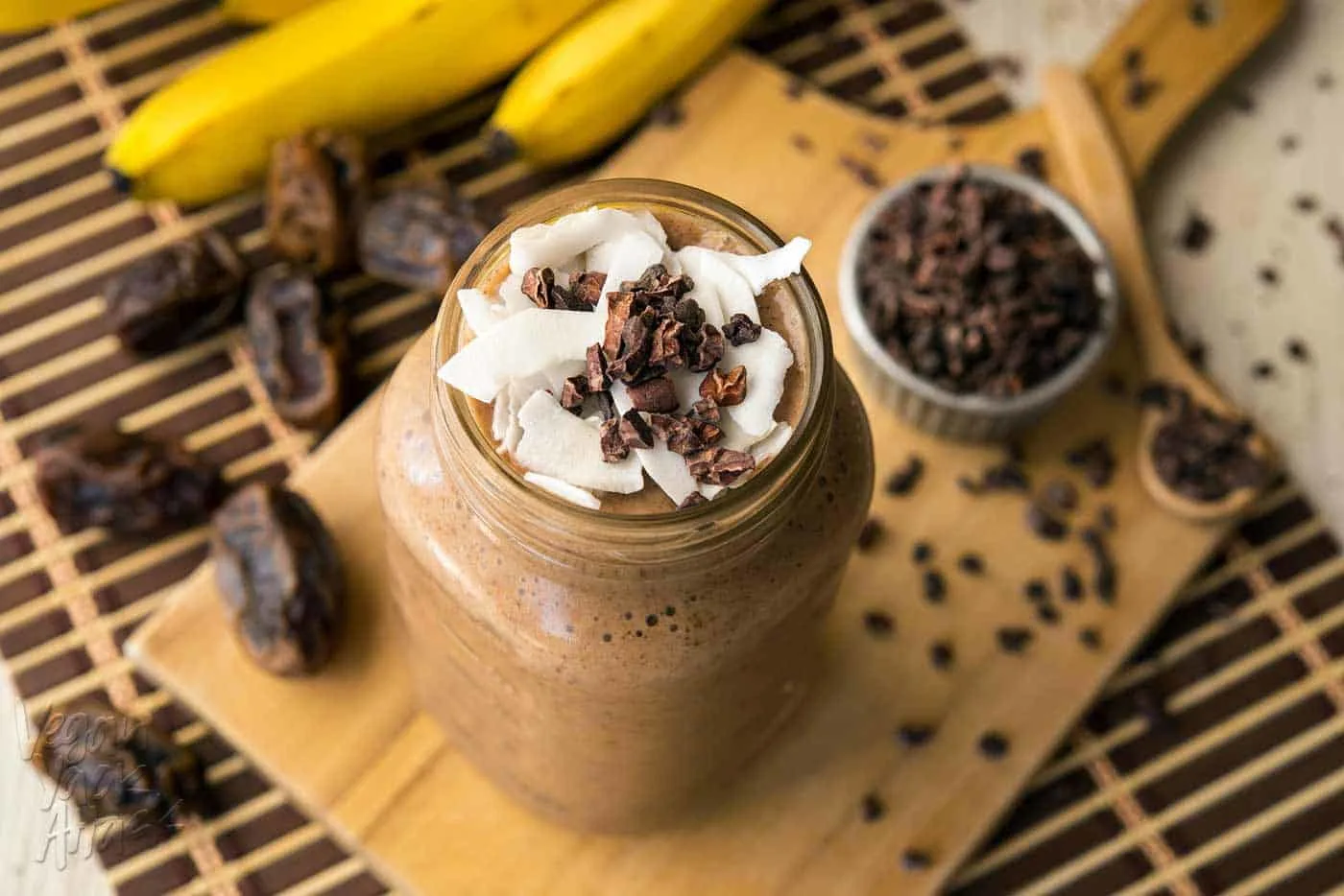 Large jar filled with banana cacao recovery smoothie, on a bread board surrounded by ingredients