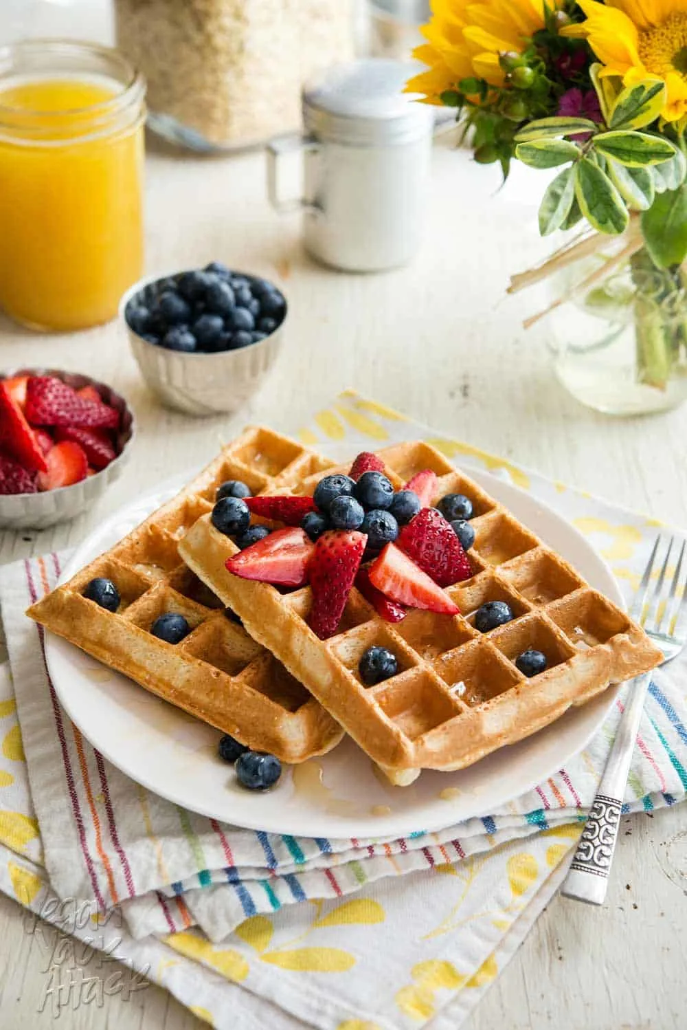 two berry pineapple belgian waffles on a white plate, topped with berries, sitting atop two colorful napkins