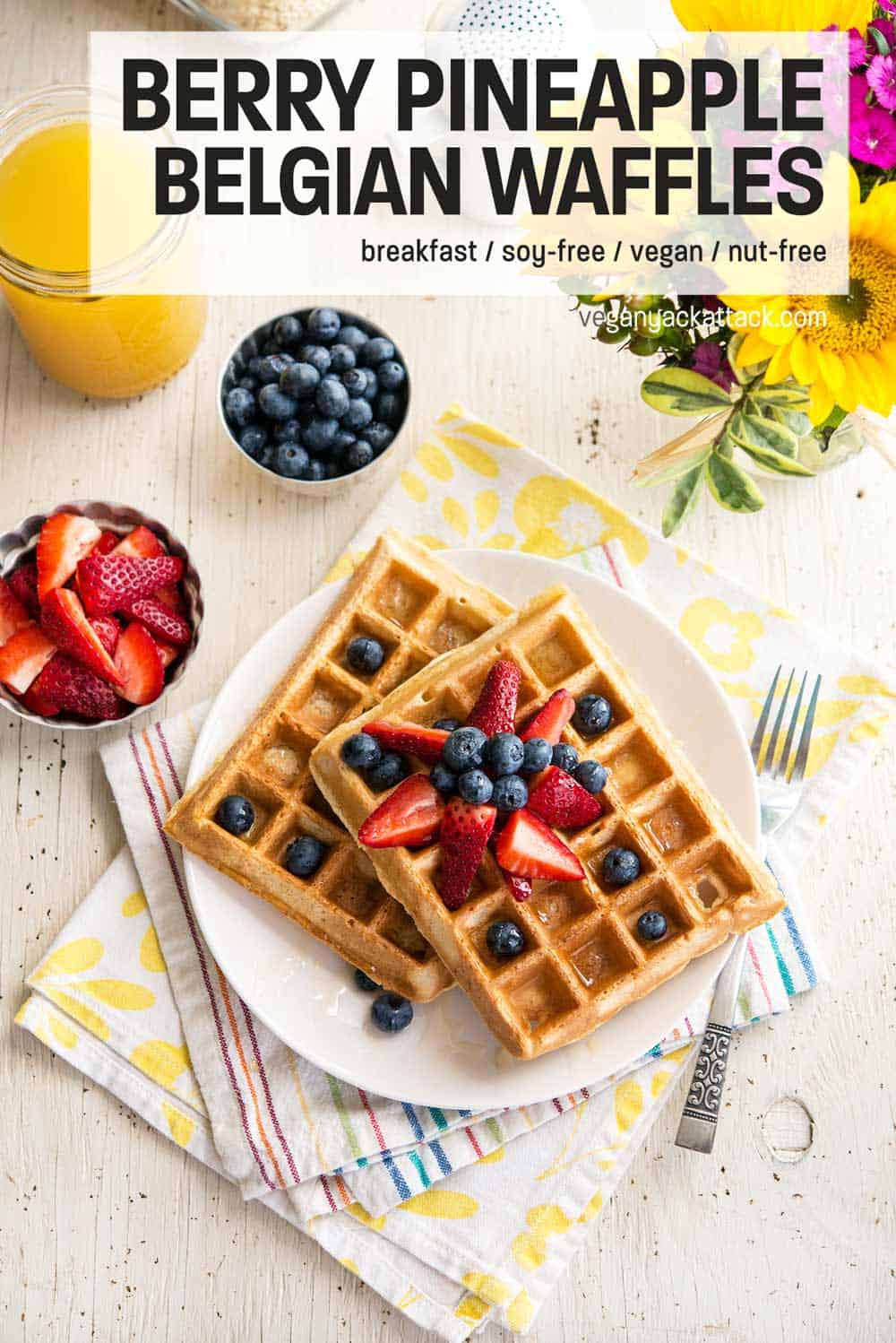 two berry pineapple belgian waffles on a white plate, topped with berries, sitting atop two colorful napkins