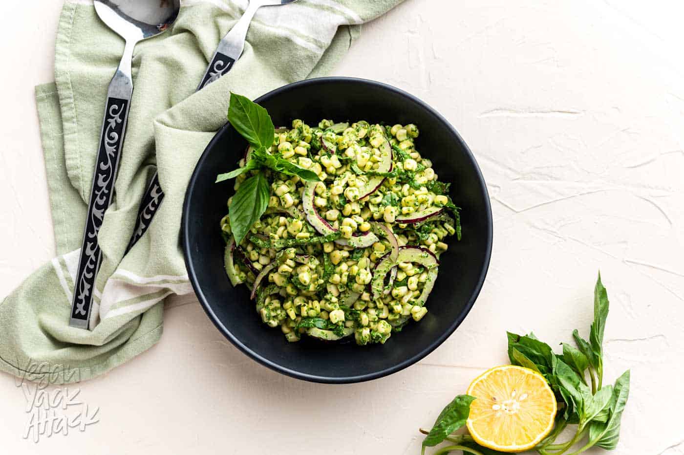 Large black bowl filled with Summer corn salad and basil pesto aioli with tongs and linen nearby