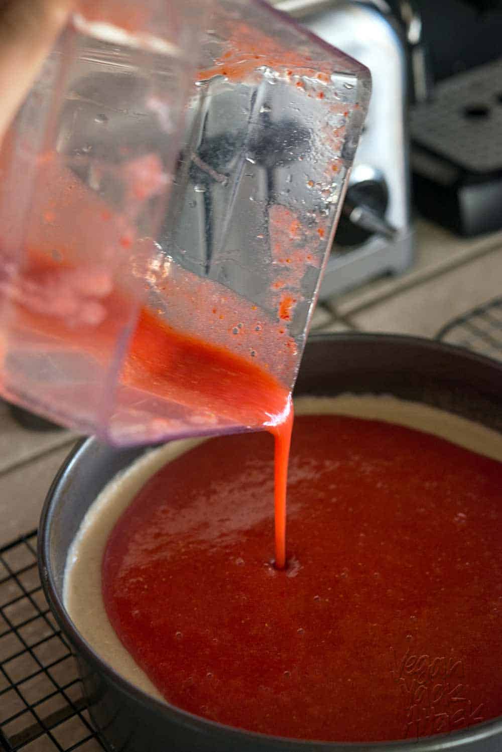Strawberry sauce being poured from blender onto cheesecake
