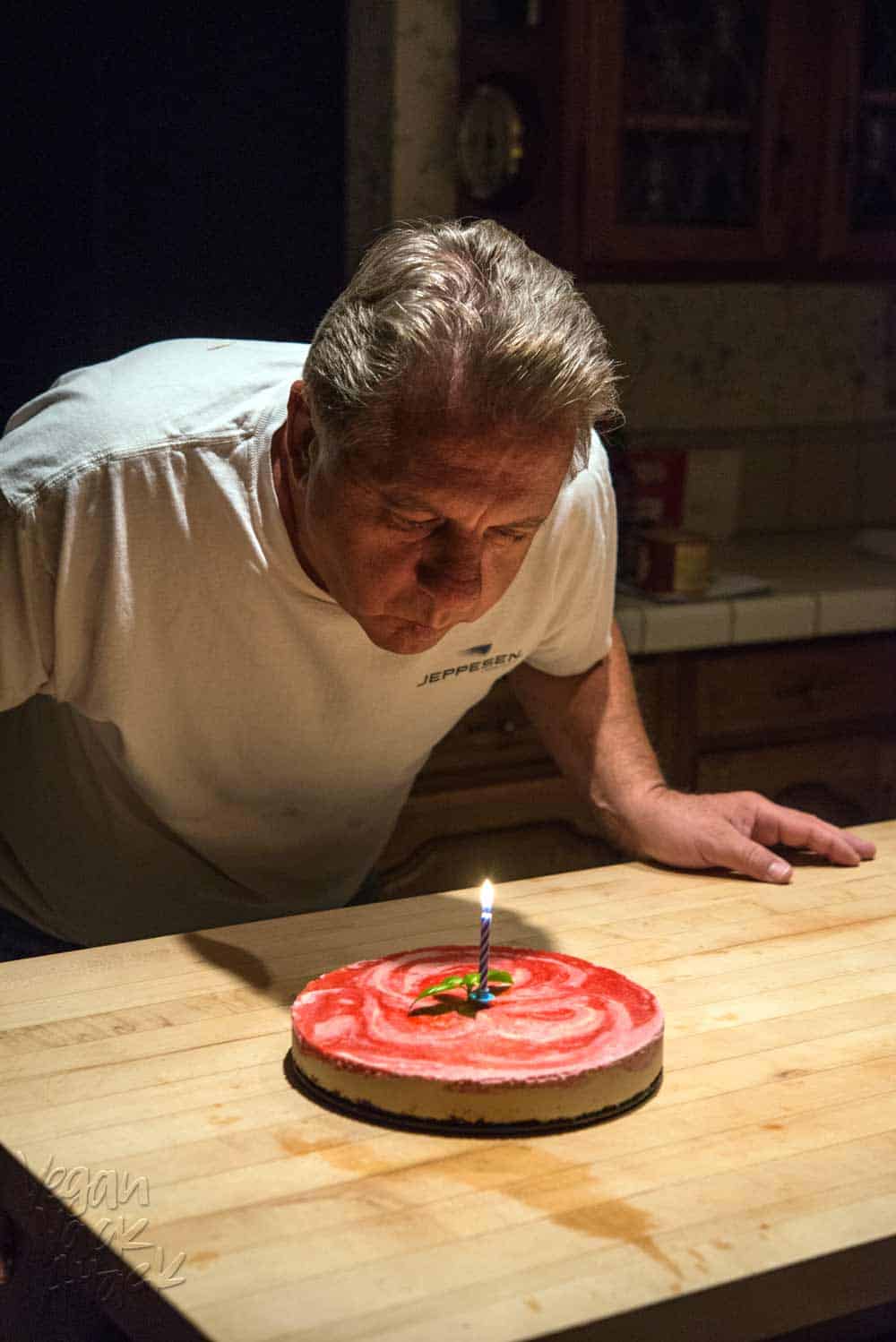 Older gentleman blowing out birthday candle on cheesecake