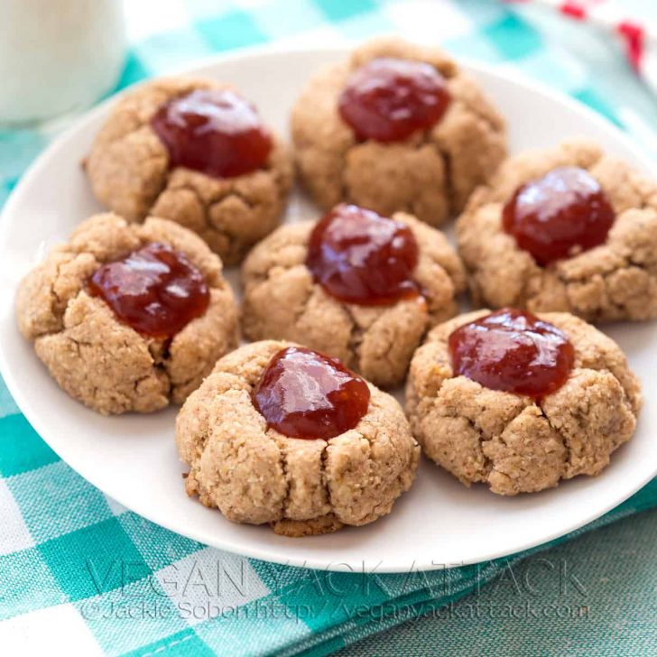 Almond butter jam thumbprint cookies on a white plate on a teal, checkered napkin