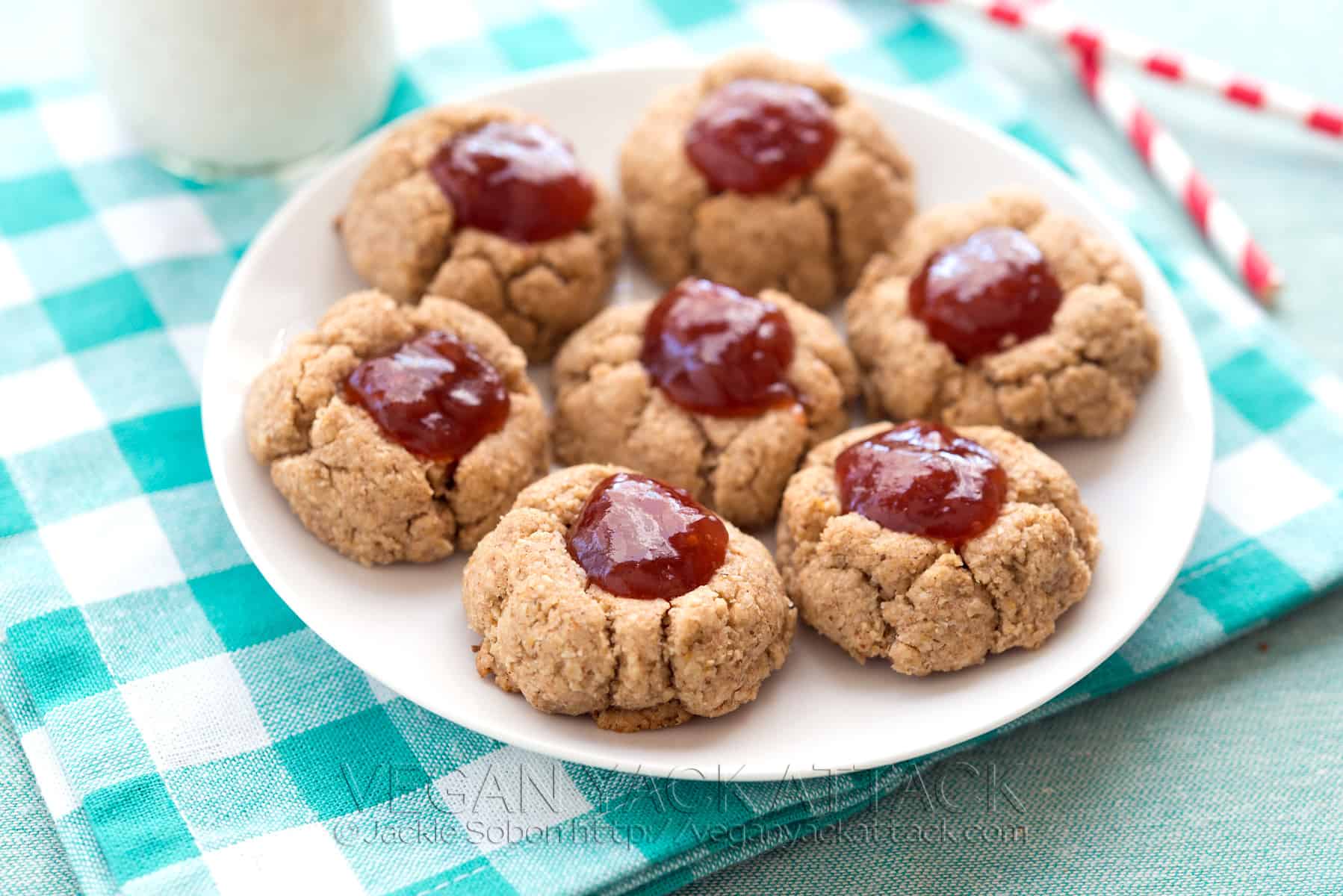 Almond butter jam thumbprint cookies on a white plate on a teal, checkered napkin