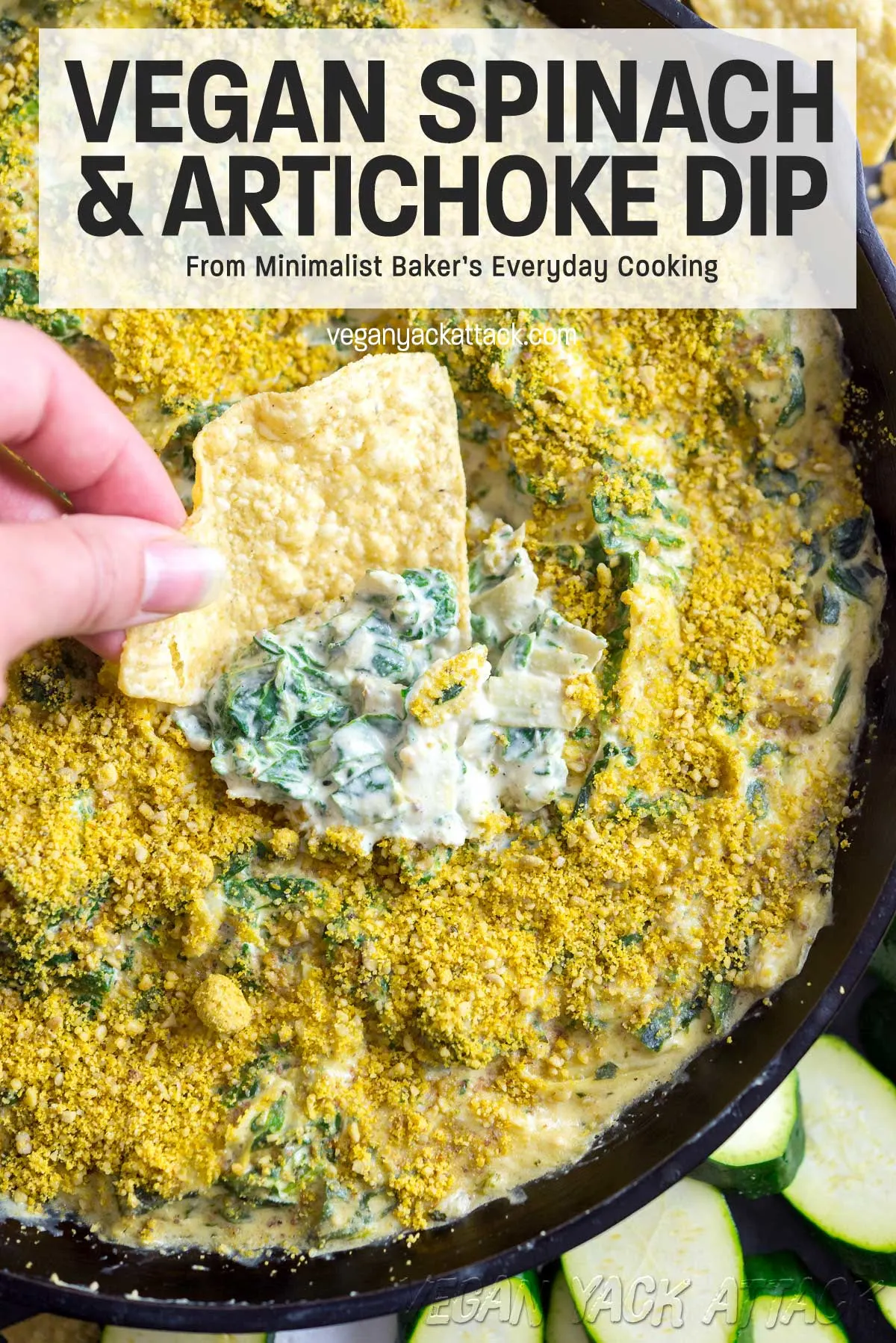 Hand dipping chip into a large cast iron skillet filled with vegan artichoke spinach dip