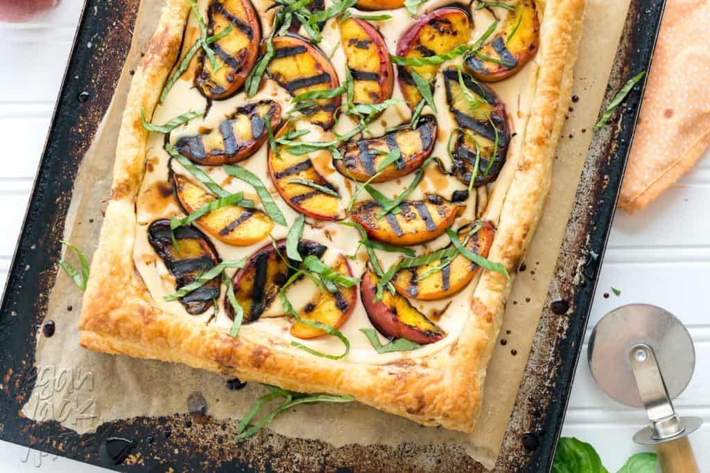 Grilled peaches and cream pastry on a baking sheet next to peaches and linen