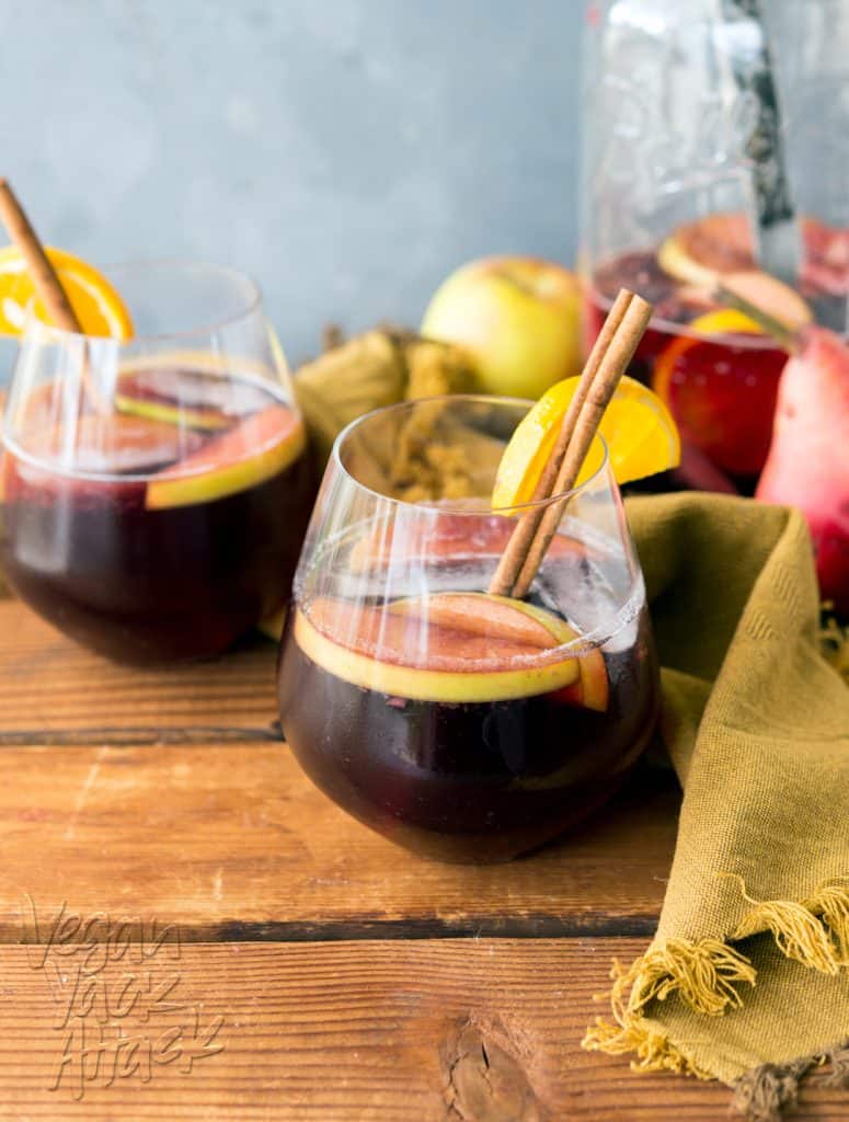 Two glasses of red fall sangria on a wood table with dark yellow linen