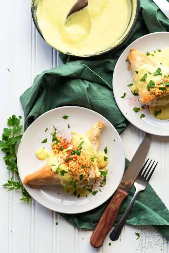two plates of fillo dough pockets covered with vegan hollandaise sauce on a green linen
