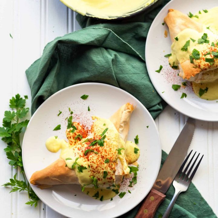 two plates of fillo dough pockets covered with vegan hollandaise sauce on a green linen