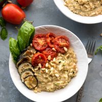 risotto in white bowl, topped with roasted zucchini and tomatoes
