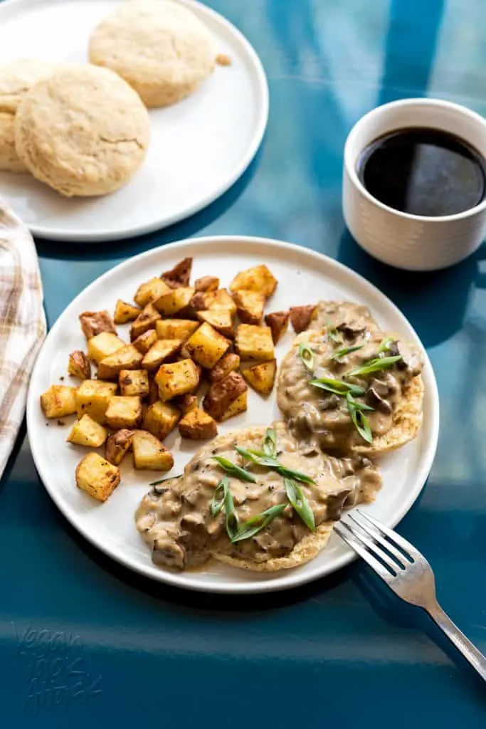 plate of biscuits and gravy with side of potatoes next to a cup of coffee on a teal tabletop