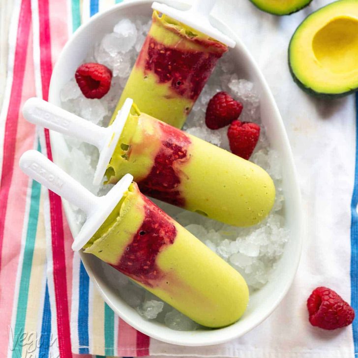 Green-hued avocado raspberry popsicles in a white dish on a striped linen