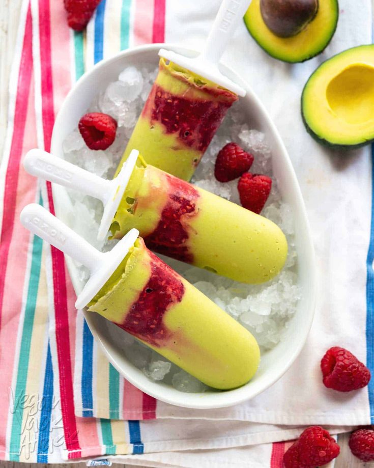 Green-hued avocado raspberry popsicles in a white dish on a striped linen