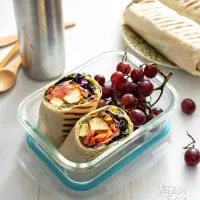 A chipotle tofu rainbow wrap cut in half in a lunch container with grapes