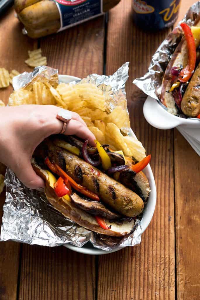 hand reaching for grilled vegan sausage in a foil-lined plate