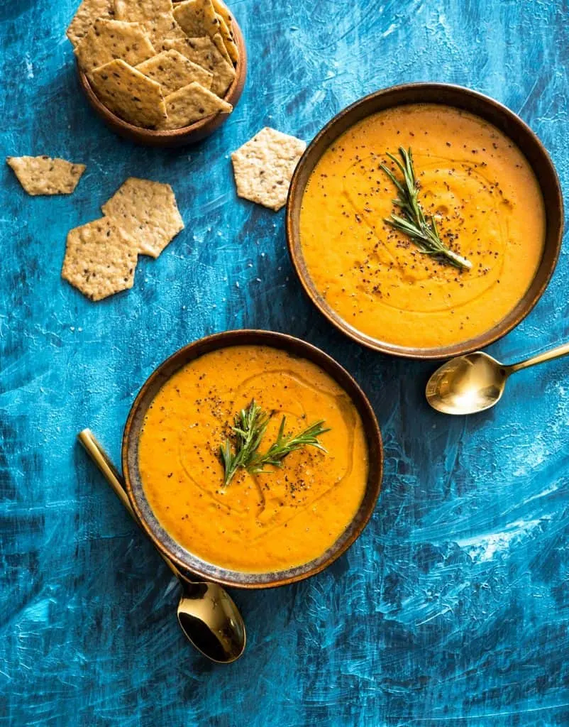 Image of two bowls of tomato bisque, with crackers on the side, on a painted blue background