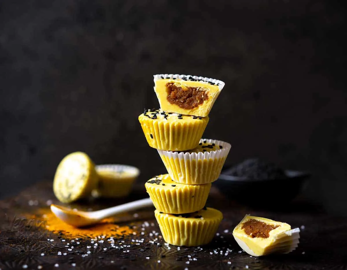 stack of yellow-hued peanut butter cups topped with black sesame seeds on a black background
