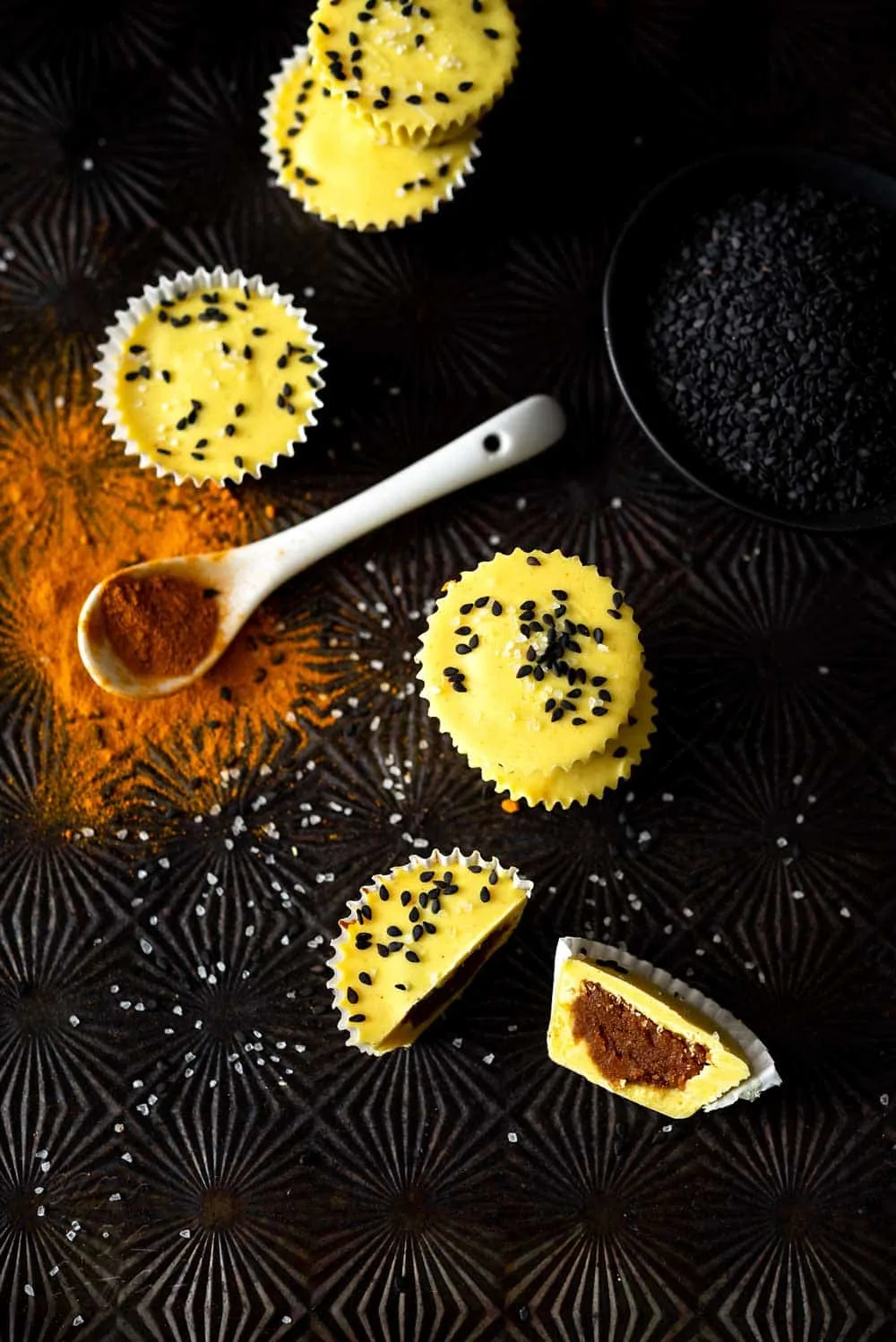 stack of yellow-hued peanut butter cups topped with black sesame seeds on a black background