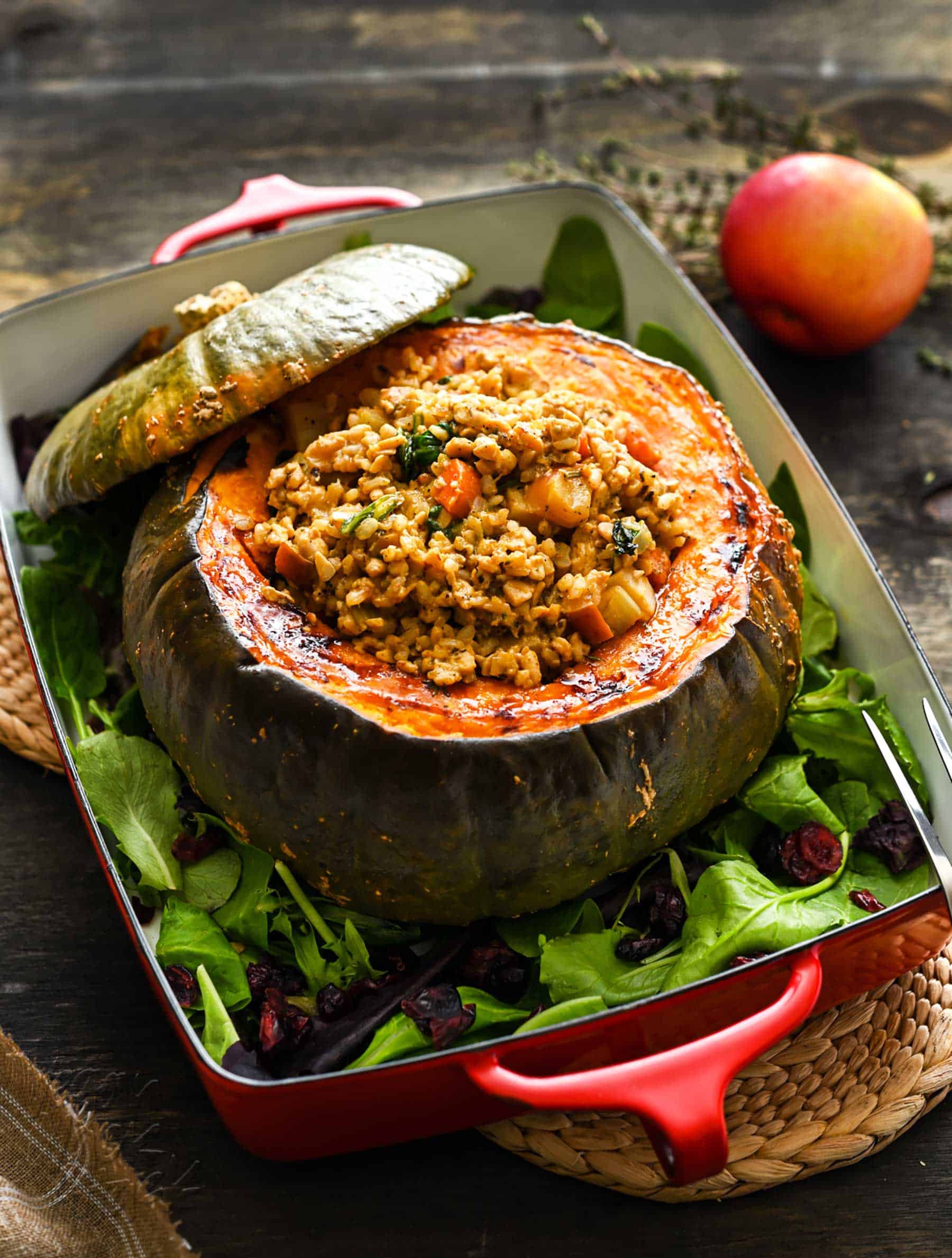 A large, roasted kabocha squash centerpiece, in a casserole dish, stuffed with a rice/tempeh mixture, on a dark background.