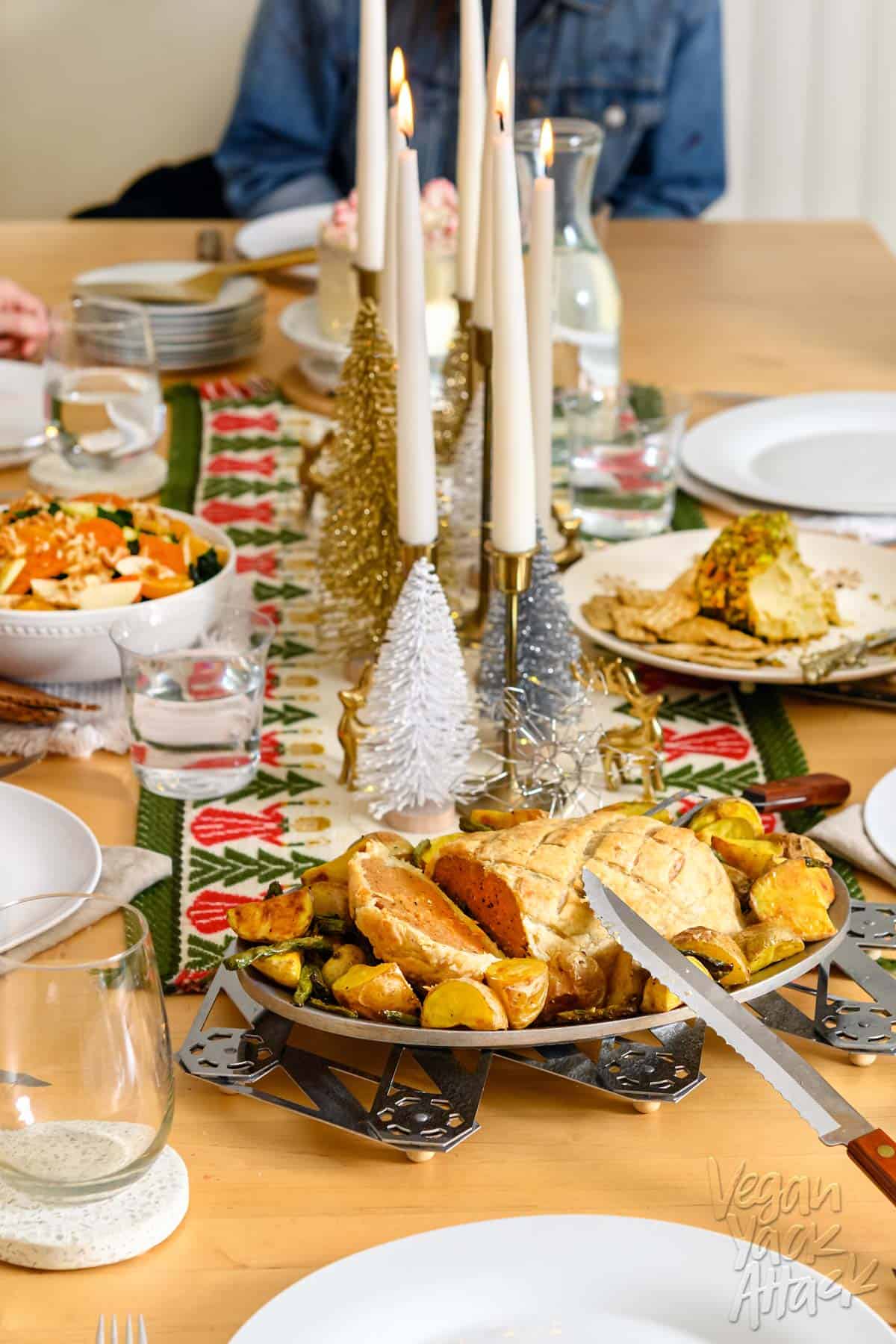 Image of an ultimate vegan holiday dinner spread with table runner and dishes, including salad and sliced seitan Wellington