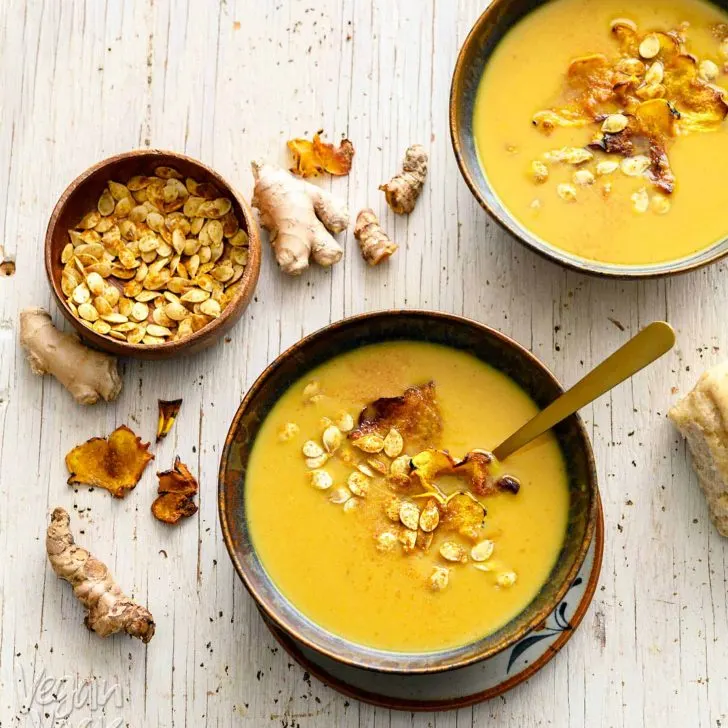 Two bowls of ginger turmeric squash soup with toasted seeds and a bread roll