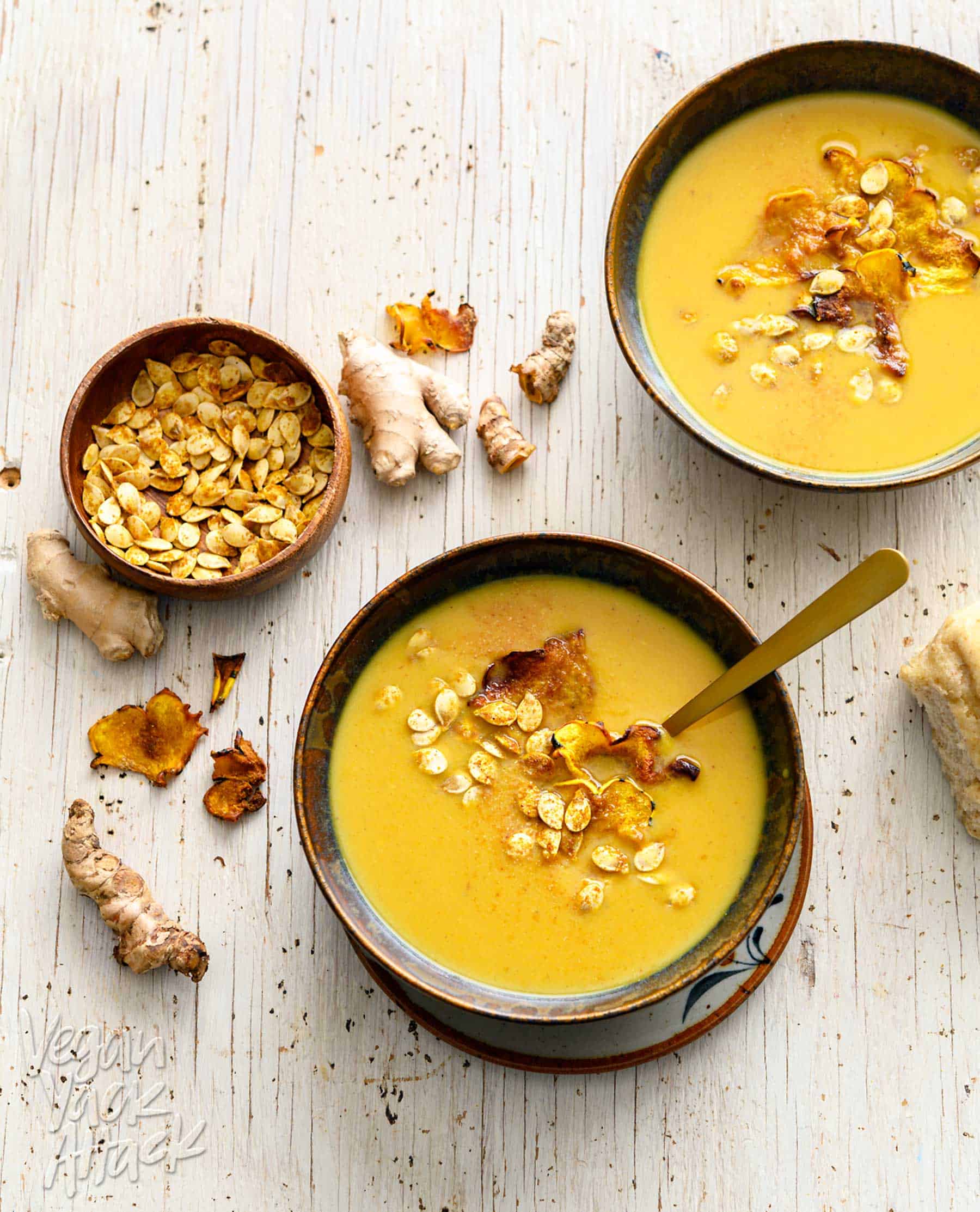 Two bowls of ginger turmeric squash soup with toasted seeds and a bread roll