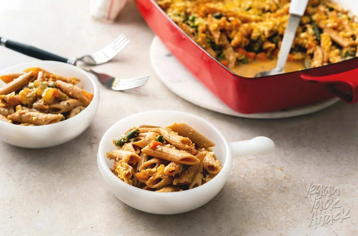 A photo of two bowls filled with vegan noodle casserole, next to a casserole dish.