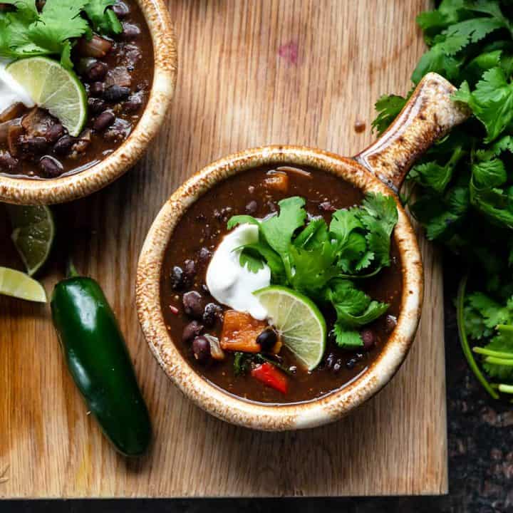 Image of two bowls of black bean stew on a cutting board with fresh cilantro bundle