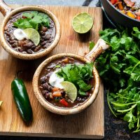 Image of two bowls of black bean stew on a cutting board with fresh cilantro bundle
