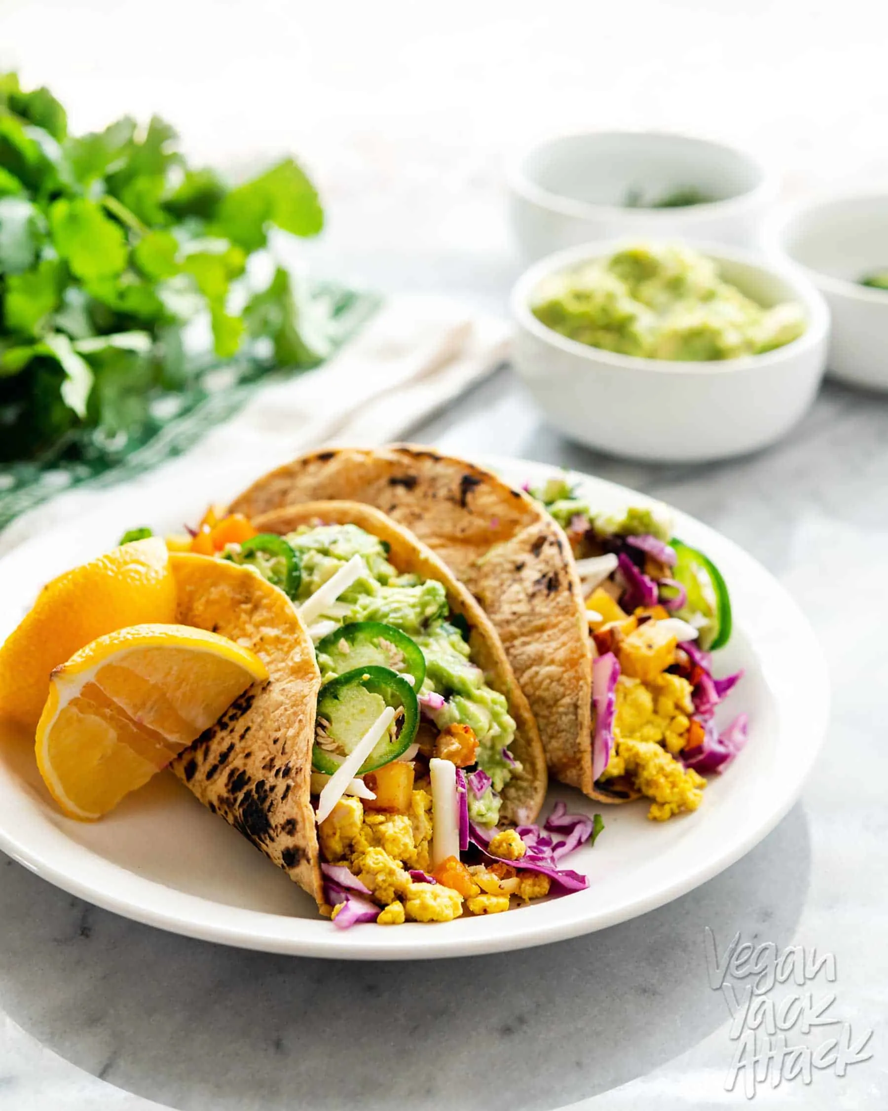 An image of vegan breakfast tacos plated, on a marble table with assorted toppings near it