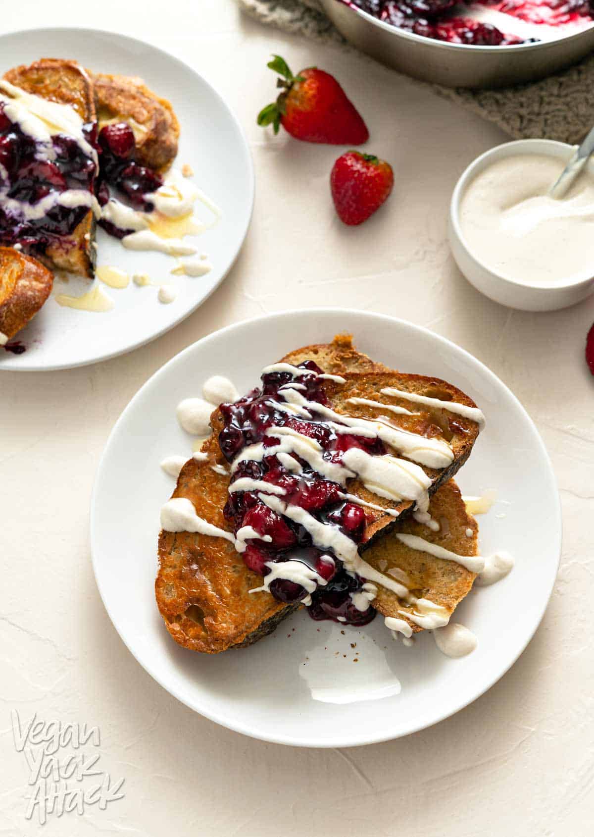 Image of two plates of berry sourdough French toast on an off-white background with cream sauce