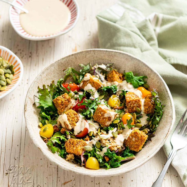 Comforting Tempeh Kale Salad in a ceramic bowl next to a green linen and fork
