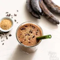 One large glass filled with chocolate sesame smoothie, with seeds, nibs, and bananas on the side