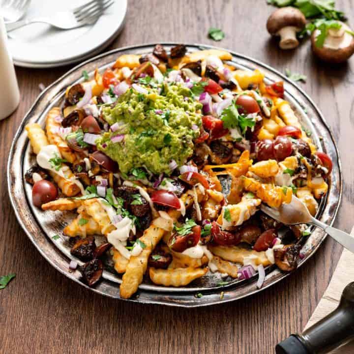 Platter of vegan mushroom asado fries on a wood table, with plates and forks