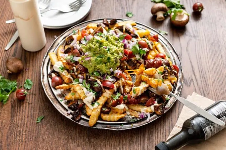 Platter of vegan mushroom asado fries on a wood table, with plates and forks