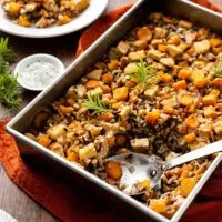 Large baking pan of squash wild rice bake on a brown wood table with rust-colored linen