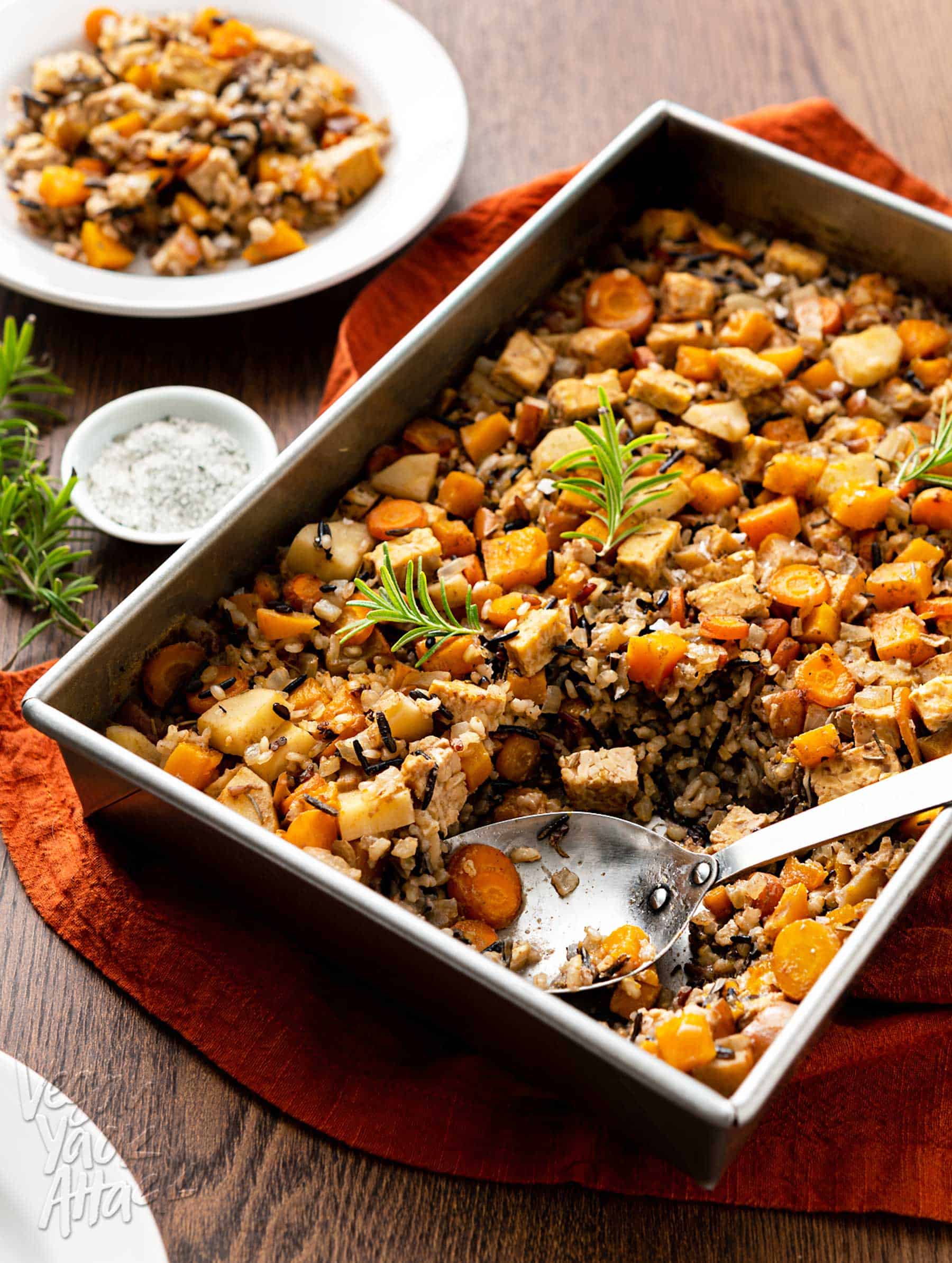 Large baking pan of squash wild rice bake on a brown wood table with rust-colored linen