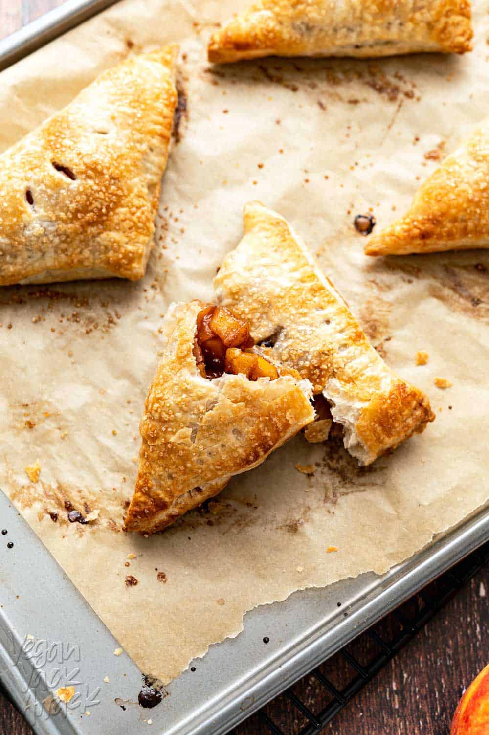 Four apple turnovers on a paper-lined baking sheet with apples