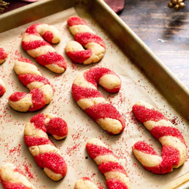 Close up of cookies shaped and striped like candy canes on a baking sheet