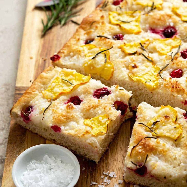 Focaccia topped with squash and cranberries on a wood cutting board